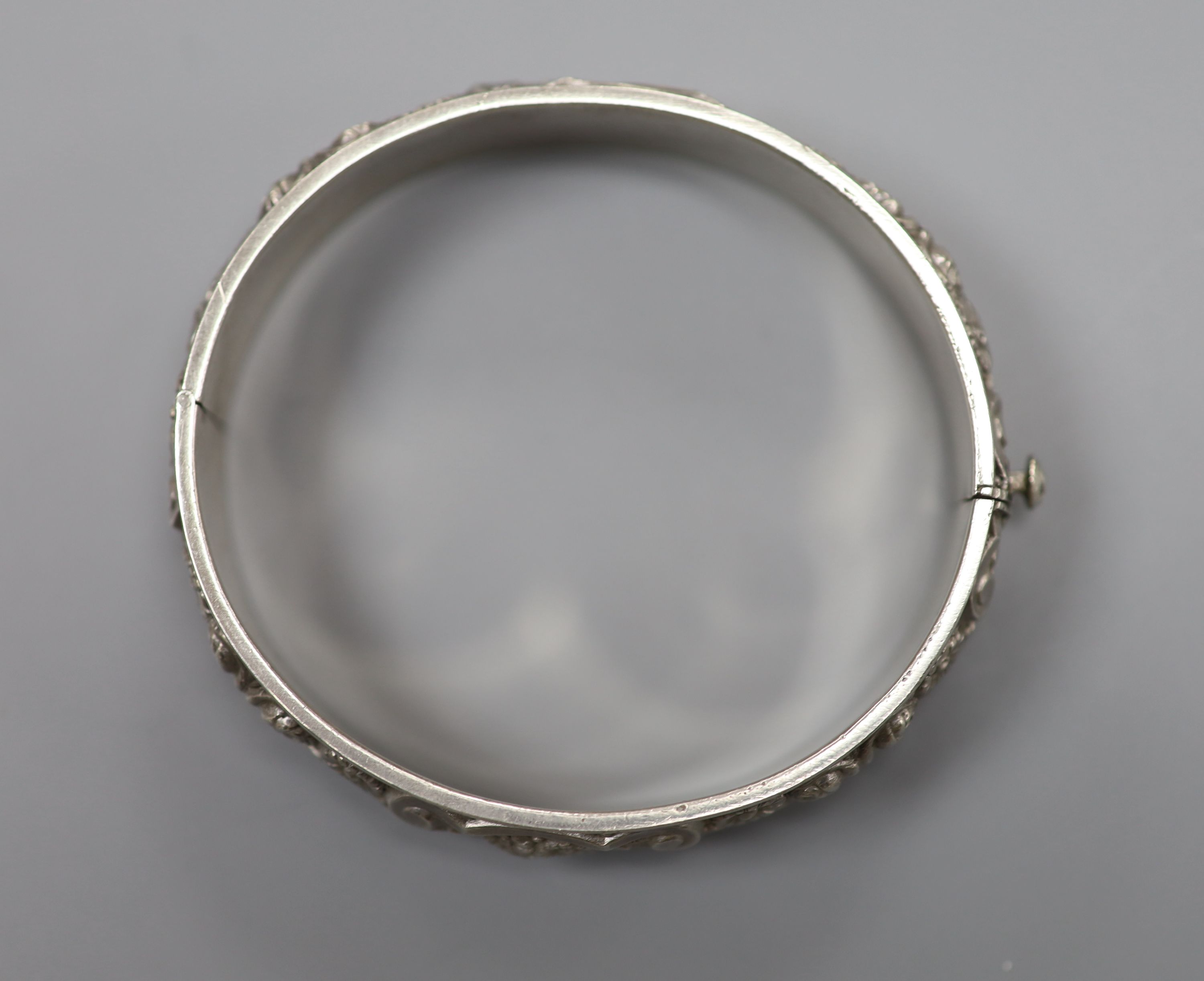 A continental white metal hinged bangle, decorated with continuous band of flowers and scrolls, 19 grams.